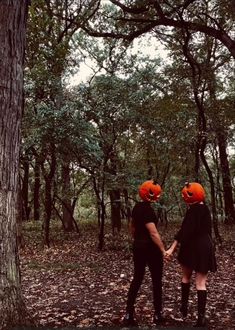 two people in halloween costumes holding hands with pumpkins on their heads and trees behind them