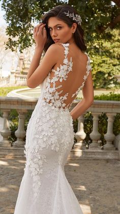 a woman in a white wedding dress with flowers on it's back, posing for the camera