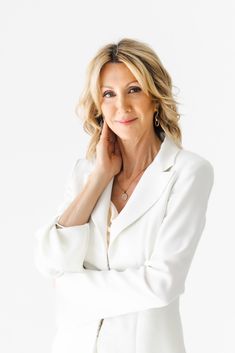 a woman in a white suit posing with her arms crossed and smiling at the camera