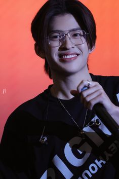 a man with glasses holding a microphone in front of an orange background and smiling at the camera