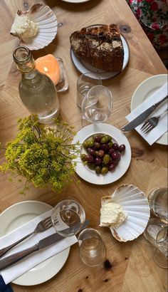 a wooden table topped with white plates and dishes filled with different types of food on top of it