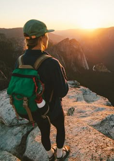 a person with a backpack standing on top of a mountain looking out at the sunset