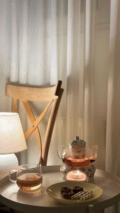 tea and cookies on a table in front of a window with white curtained drapes