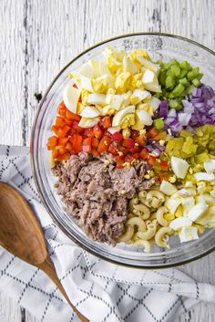 a bowl filled with pasta, meat and veggies next to a wooden spoon