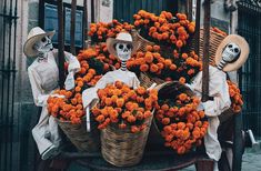 two skeletons are sitting on a carriage with orange flowers in the basket and another skeleton is standing next to them