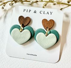 two heart shaped wooden earrings on top of a piece of white and green paper with gold hardware