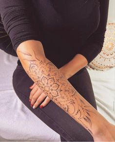 a woman sitting on top of a bed with her arm covered in hendi tattoos