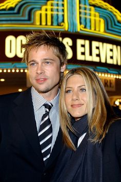 a man and woman standing in front of a theater marquee with lights on