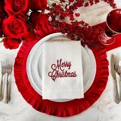 a table setting with red roses, silverware and merry christmas written on napkins