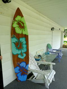 a surfboard sitting on the side of a building next to lawn chairs and tables