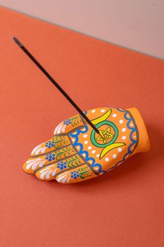 an orange and blue hand holding a black stick on top of a red surface with white dots