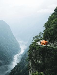 an orange tent sitting on top of a cliff next to a river in the mountains