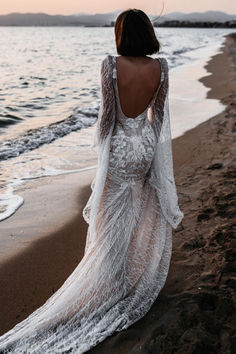 a woman standing on top of a beach next to the ocean wearing a white dress