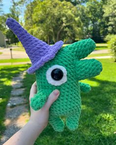 a hand holding a green stuffed animal with a purple hat