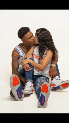 a man and woman sitting next to each other on top of a white floor kissing