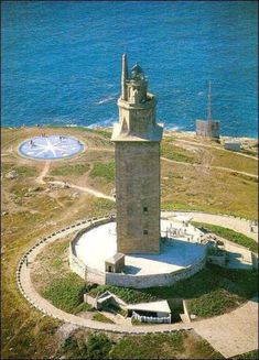 an aerial view of a clock tower in the middle of a grassy area next to the ocean