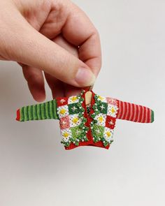 someone is holding an ornament in the shape of a christmas sweater with flowers on it