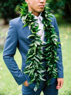 a man wearing a blue suit and green leaves around his neck is standing in the grass