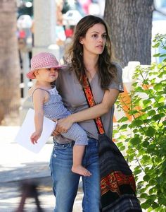 a woman holding a baby in her arms while walking down the street with another child