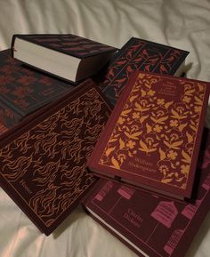 four different colored books on a bed with white sheets in the foreground and one red book laying on top of each other