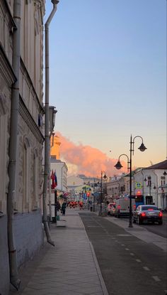 a city street with cars parked on the side and people walking down the sidewalk at sunset