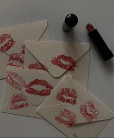 four envelopes with red glittered lips on them and a lipstick bottle next to it