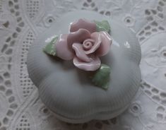 a white box with a pink rose on it sitting on a lace doily covered tablecloth