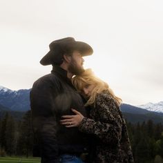 a man and woman standing next to each other with mountains in the backgroud