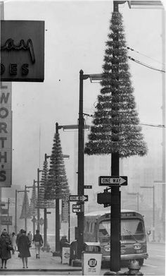 a black and white photo of people walking down the street in front of a christmas tree