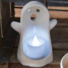 a small white candle holder with a lit candle in it's center, sitting on the ground