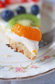 a piece of cake on a plate with fruit in the background and a fork stuck into it