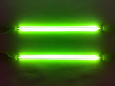 two neon lights are glowing green on a dark background with wires running through the middle