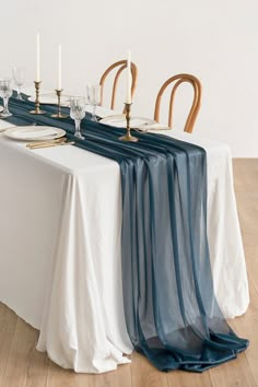 the table is set with white plates and silverware, blue sheer cloth draped over it