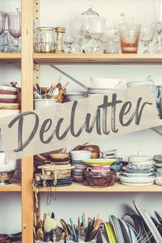 a wooden sign that says declutter sitting on top of a shelf filled with dishes