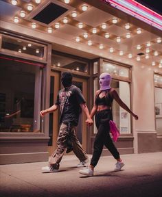 two people are walking down the street in front of a building with marquee lights