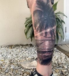 a man's leg with a palm tree and beach scene tattoo on his calf