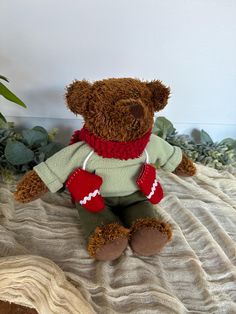 a brown teddy bear sitting on top of a bed next to a potted plant