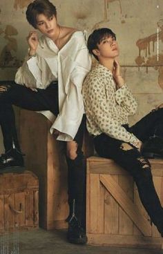 two young men sitting on top of wooden boxes in front of a wall with peeling paint