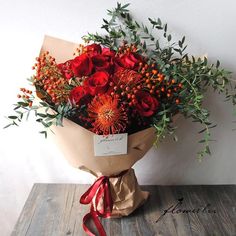 a bouquet of red flowers and greenery wrapped in brown paper on a wooden table