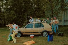 a group of people standing around a car in the grass with one person holding a frisbee