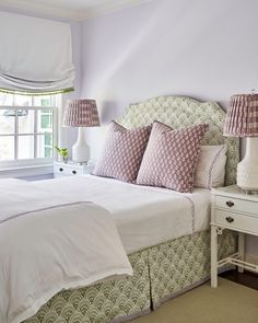 a white bed topped with lots of pillows next to a window