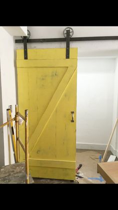 a yellow barn door is open in a room with tools and construction materials on the floor