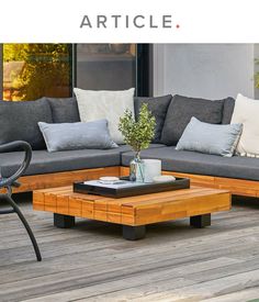 a couch and coffee table on a wooden deck with plants in vases next to it