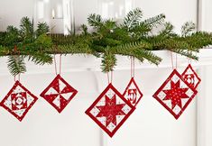 three red ornaments hanging from a mantel with pine branches and candles in the background