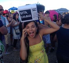 a woman in a yellow dress holds up a sign while talking on her cell phone