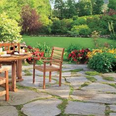 a table and chairs sitting on top of a stone floor next to a lush green field