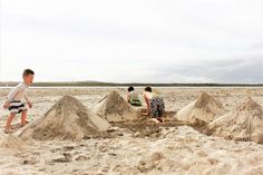 children playing in the sand on a beach with many piles of sand and one boy is digging