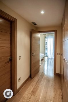 an empty hallway leading to a bedroom with wood floors and white curtains on the windows