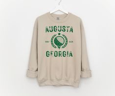 Vintage Augusta Georgia Golf with golf club on a crewneck sweatshirt.  The design will be printed as shown.  The color sweatshirt in the picture is sand.  You can pick your color of ink for the design printed. To order your sweatshirt please pick the sweatshirt color and size. The blank sweatshirts are Jerzees brand and are 50/50 cotton and polyester.  These are unisex sizing so please check the sizing chart in the pictures.  Size up for an oversized fit.   Care- Wash inside out in cold water, tumble dry on low.  Do not dry clean. Primary Color option is the shirt.   No returns or exchanges on customized items. Please contact me at any time for concerns about your purchase. Cotton Long Sleeve Golf Sweatshirt, Sporty Letter Print Sweatshirt For Golf, Green Crew Neck Sweatshirt For Sports Season, Casual Golf Sweatshirt With Crew Neck, Sporty Crew Neck Golf Sweatshirt, Sporty Crew Neck Sweatshirt For Golf, Sporty Long Sleeve Sweatshirt For Golf, Augusta Golf, Golf Sweatshirt