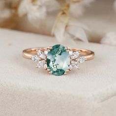 an oval cut green and white diamond ring on top of a flowered cloth with flowers in the background